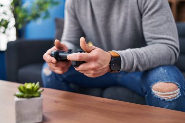 Young latin man playing video game sitting on sofa at home
