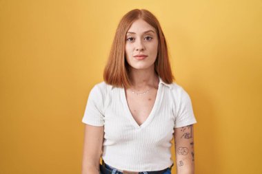 Sarı arka planda duran genç kızıl saçlı kadın yüzünde ciddi bir ifadeyle rahatlamış. Basit ve doğal bir şekilde kameraya bakıyorsun.. 