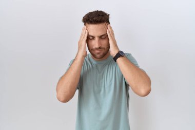 Beyaz arka planda duran sakallı İspanyol bir adam, eli başının üstünde, stres yüzünden başı ağrıyor. migren ağrısı. 