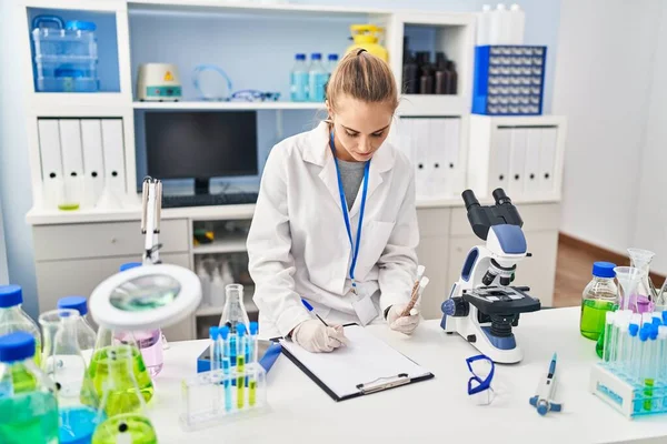 Young Blonde Woman Wearing Scientist Uniform Holding Test Tubes Writing — 스톡 사진