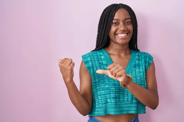 年轻的非洲裔美国人 辫子耸立在粉色背景之上 手背朝后 竖起大拇指 带着自信的笑容 — 图库照片