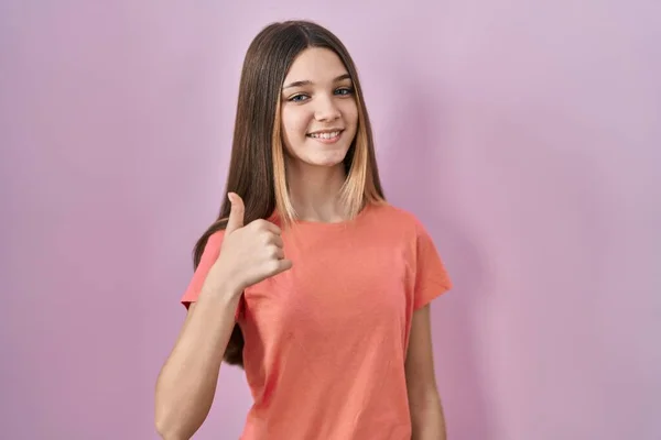 少女站在粉红的背景上 用手拿着快乐的大拇指做手势 赞成的表情看着相机显示的成功 — 图库照片