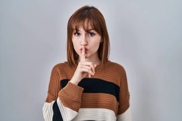 孤立した背景に縞模様のセーターを着た若い美しい女性が唇に指で静かにするように求めています 沈黙と秘密の概念 — ストック写真
