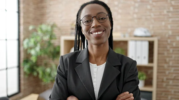 アフリカ系アメリカ人女性ビジネスワーカー笑顔自信を持って立ってとともに腕交差ジェスチャーでオフィス — ストック写真