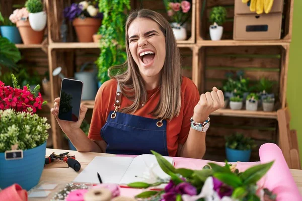 スマートフォンの画面を示す花屋で働くヒスパニック系の若い女性は誇りに思って叫んで 勝利と成功を祝う非常に興奮して腕を上げ — ストック写真