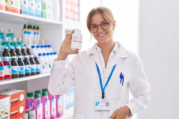 Młoda Blondynka Dziewczyna Farmaceuta Uśmiecha Się Pewnie Trzymając Butelkę Tabletek — Zdjęcie stockowe