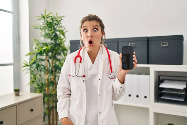 Ung Kvinna Bär Läkare Uniform Hålla Smartphone Rädd Och Förvånad — Stockfoto