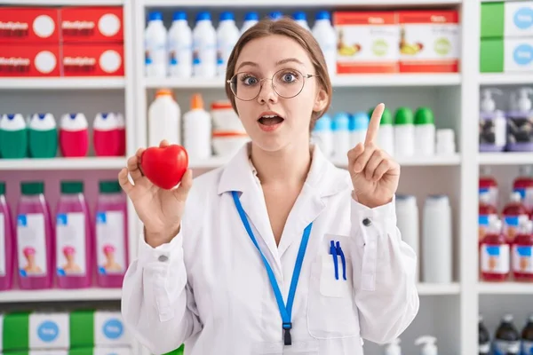 Молодая Белая Женщина Работающая Аптеке Держит Красное Сердце Улыбаясь Идеей — стоковое фото