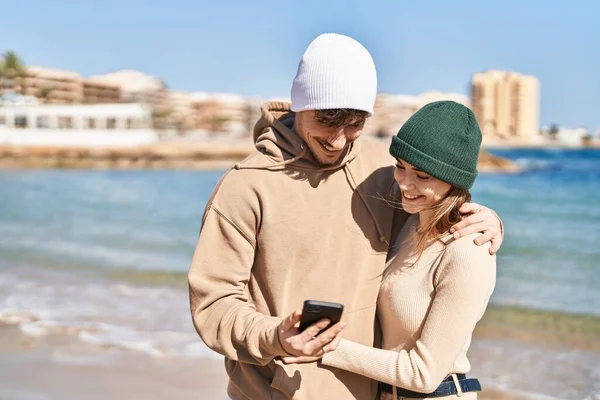 夫婦は海辺でスマートフォンを使って抱き合っている — ストック写真