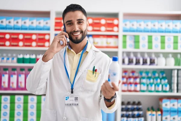 Hombre Árabe Joven Farmacéutico Sosteniendo Botella Medicamento Hablando Teléfono Inteligente — Foto de Stock