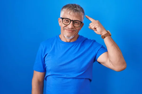 一个白发苍苍的西班牙男人站在蓝色的背景上微笑着 用一个手指指着头 伟大的想法或想法 美好的回忆 — 图库照片