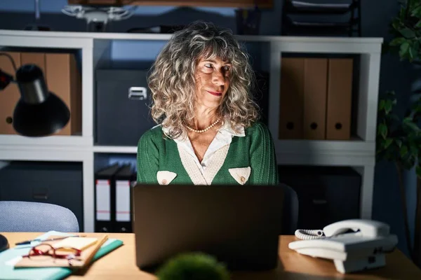 顔に笑顔で横に離れて見て コンピュータのラップトップを使用して夜に働く中年の女性は 自然な表現 自信を持って — ストック写真