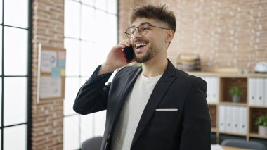 Genç Arap iş adamı gülümseyerek ofisteki akıllı telefondan konuşuyor.