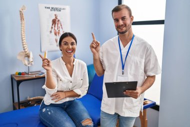 Fizyoterapist randevusunda, yüzünde kocaman bir gülümsemeyle elini kameraya doğru gösteren genç bir İspanyol kadın.. 