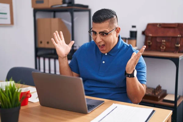 ラップトップでオフィスで働いている若いヒスパニック系の男は狂気を祝い 腕を上げて興奮して叫んで目を開けて成功したことに驚いています 勝者のコンセプト — ストック写真