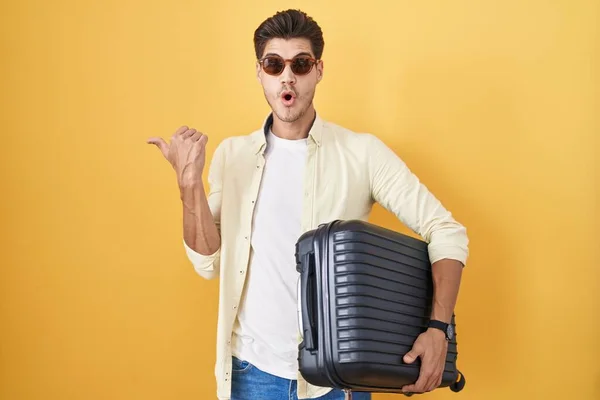 若いですヒスパニック系の男保持スーツケース夏休みに行く驚くべきポインティングとともに手指で側面 口を開けて驚くような式 — ストック写真