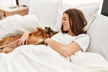 Genç İspanyol kadın yatak odasında köpeğe sarılıyor.