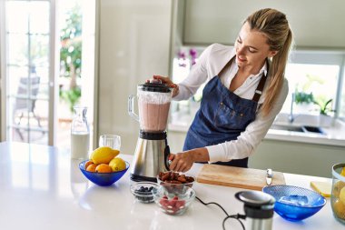 Genç sarışın kadın gülümsüyor. Kendine güveni tam. Smoothie 'yi sıvılaştırıyor.