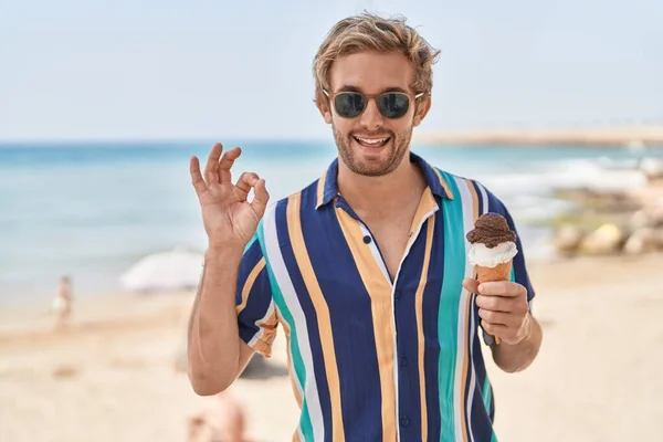 白种人在海滩上吃着冰激凌 用手指做手势 友善地微笑着 表示出极好的象征 — 图库照片