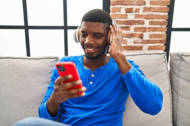 Young african american man listening to music sitting on sofa at home