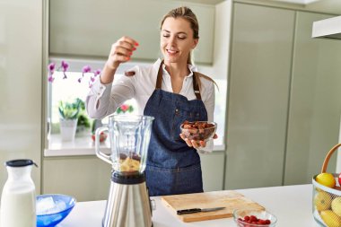 Genç sarışın kadın gülümsüyor. Mutfaktaki mikserin üzerine kendinden emin tarihler döküyor.