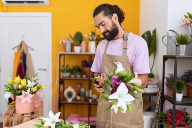 Young hispanic man florist cutting stem of flowers at flower shop