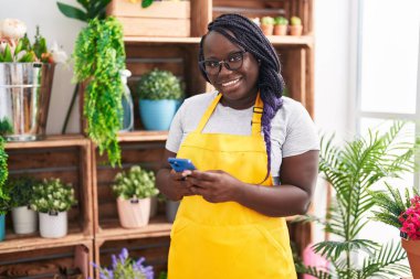 Afrikalı Amerikalı kadın çiçekçi çiçekçiye akıllı telefon kullanarak gülümsüyor.