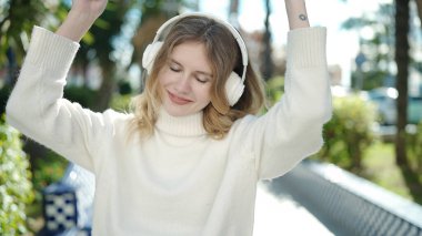 Young blonde woman listening to music and dancing at park