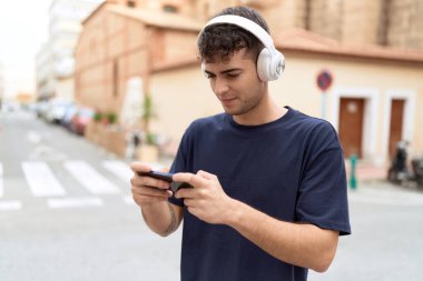 Young hispanic man smiling confident playing video game at street