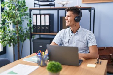 Ofiste çalışan genç İspanyol bir adam kulaklık takıyor. Yüzünde gülümsemeyle yan yana bakıyor. Doğal bir ifade. Kendinden emin gülen. 