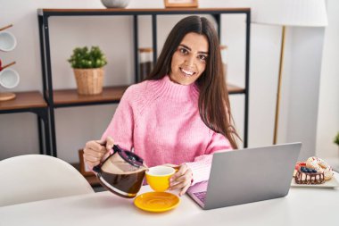 Young hispanic woman having breakfast using laptop at home