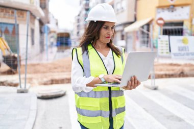 Young beautiful hispanic woman architect using laptop at street