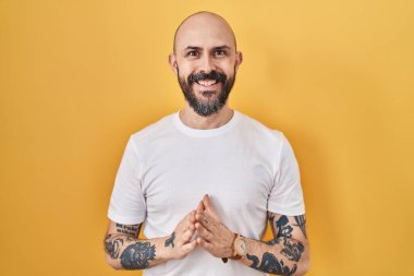 Sarı arka planda dövmeleri olan genç İspanyol adam el ele tutuşup gülümseyerek gevşemiş ve neşeliydi. Başarı ve iyimserlik 