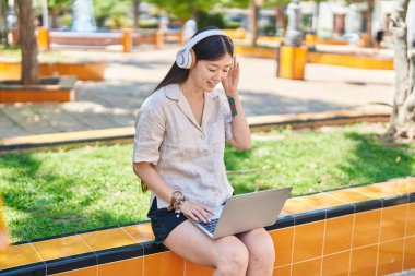 Chinese woman listening to music sitting on bench at park