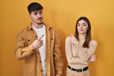 Sarı arka planda dikilen genç İspanyol çift el parmaklarıyla reklamı gösteriyor, ciddi ve sakin bir yüz. 