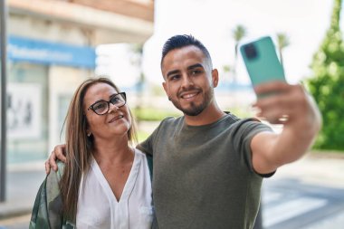 Kadın, erkek, anne ve kız sokakta akıllı telefondan selfie çekiyorlar.