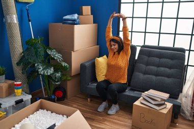 Genç Latin kadın yeni evindeki kanepede rahatça kollarını açıyor.