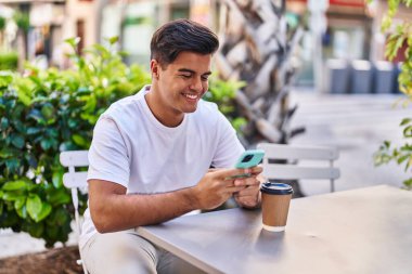 Genç İspanyol adam akıllı telefon kullanıyor. Kahve dükkanının terasında kahve içiyor.