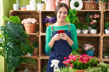 Çiçekçide akıllı telefon kullanarak gülümseyen güzel İspanyol kadın.