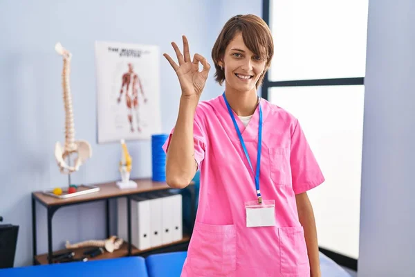 Brunetka Pracująca Klinice Rehabilitacyjnej Uśmiecha Się Pozytywnie Robiąc Znak Dłońmi — Zdjęcie stockowe
