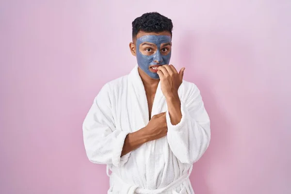 美顔マスクとバスローブを身に着けている若いヒスパニック系の男は 口の中に爪をかむ上で手で強調し 緊張している 不安の問題 — ストック写真