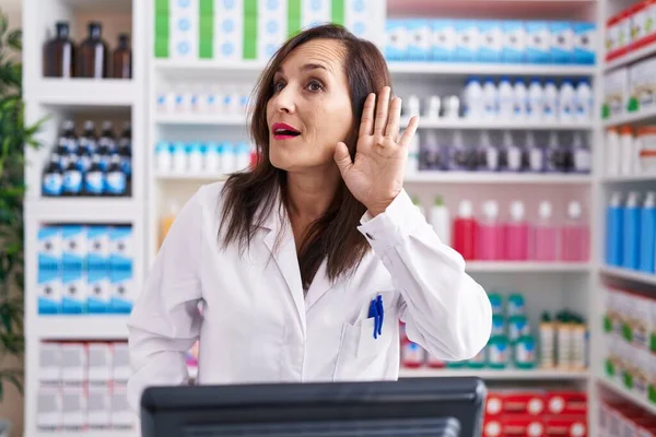 薬局で働く中世のブルネットの女性は噂やゴシップに耳を傾けながら手で笑っています 聴覚障害の概念 — ストック写真