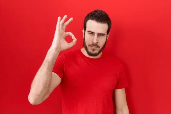 Gündelik Kırmızı Tişört Giyen Genç Spanyol Adam Gülümsüyor Parmaklarıyla Tamam — Stok fotoğraf