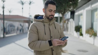 Genç İspanyol adam akıllı telefon kullanıyor. Sokakta ciddi bir ifadesi var.