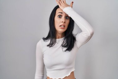 Hispanic woman standing over isolated background surprised with hand on head for mistake, remember error. forgot, bad memory concept. 