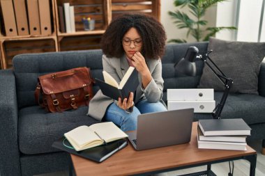 Young african american woman psychologist using laptop and reading book at psychology center