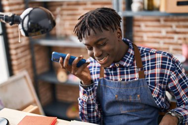 Afrikalı Amerikalı sanatçı gülümsüyor. Sanat stüdyosunda akıllı telefondan konuşuyor.