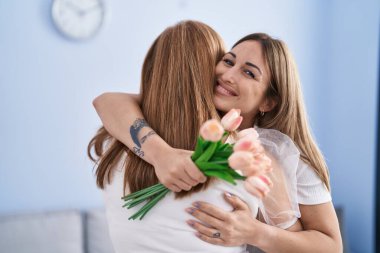 Mother and daughter surprise with flowers hugging each other at home