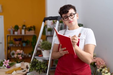 Non binary man florist writing on notebook with serious expression at flower shop
