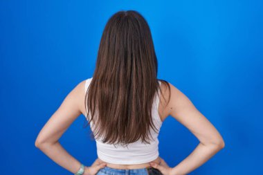 Young caucasian woman standing over blue background standing backwards looking away with arms on body 